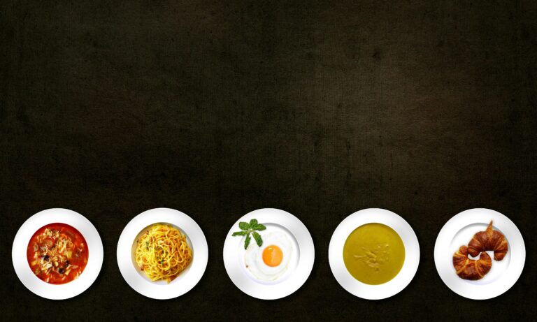 Flatlay of various dishes including pasta, egg, soup, and croissant on textured background.